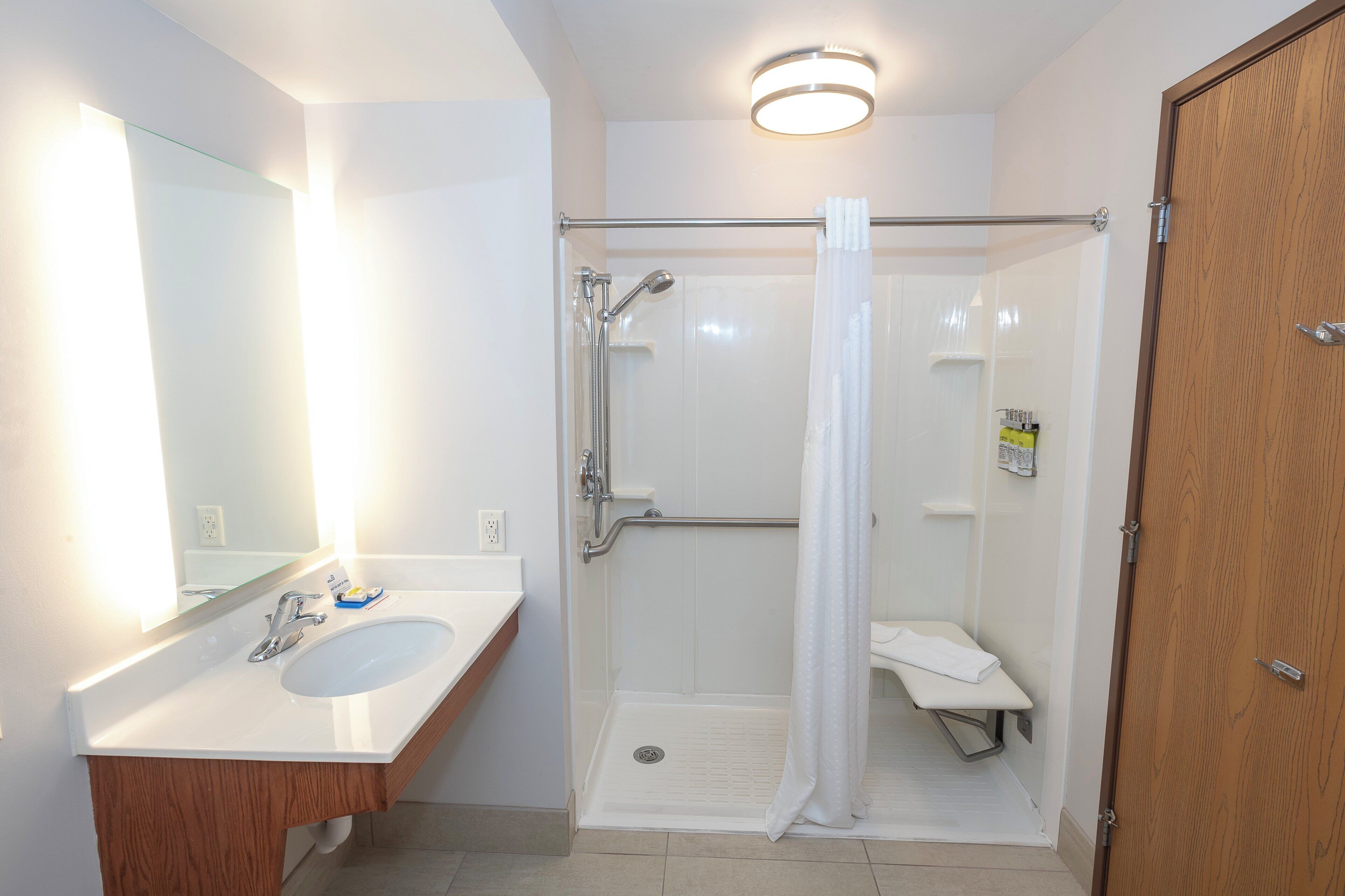 Un baño con lavamanos blanco, espejo, ducha con puerta de cristal y puerta de madera.