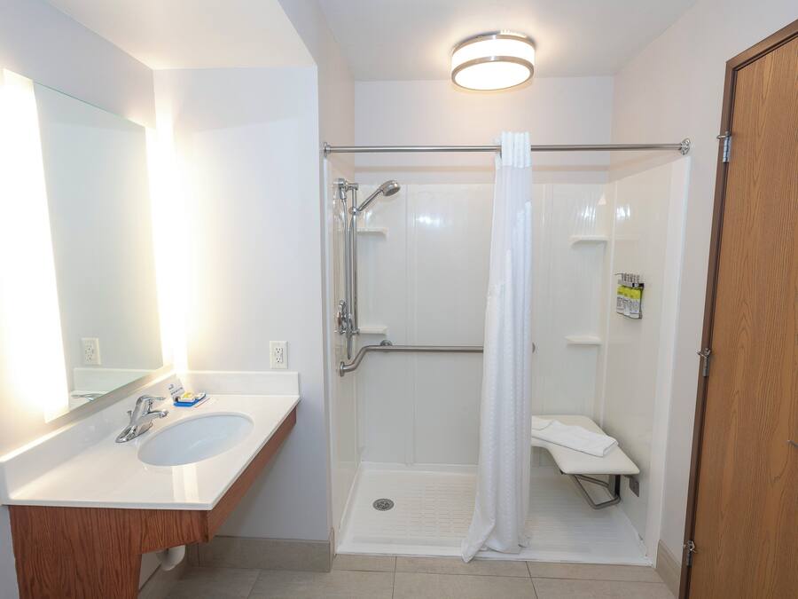 Un baño con lavamanos blanco, espejo, ducha con puerta de cristal y puerta de madera.