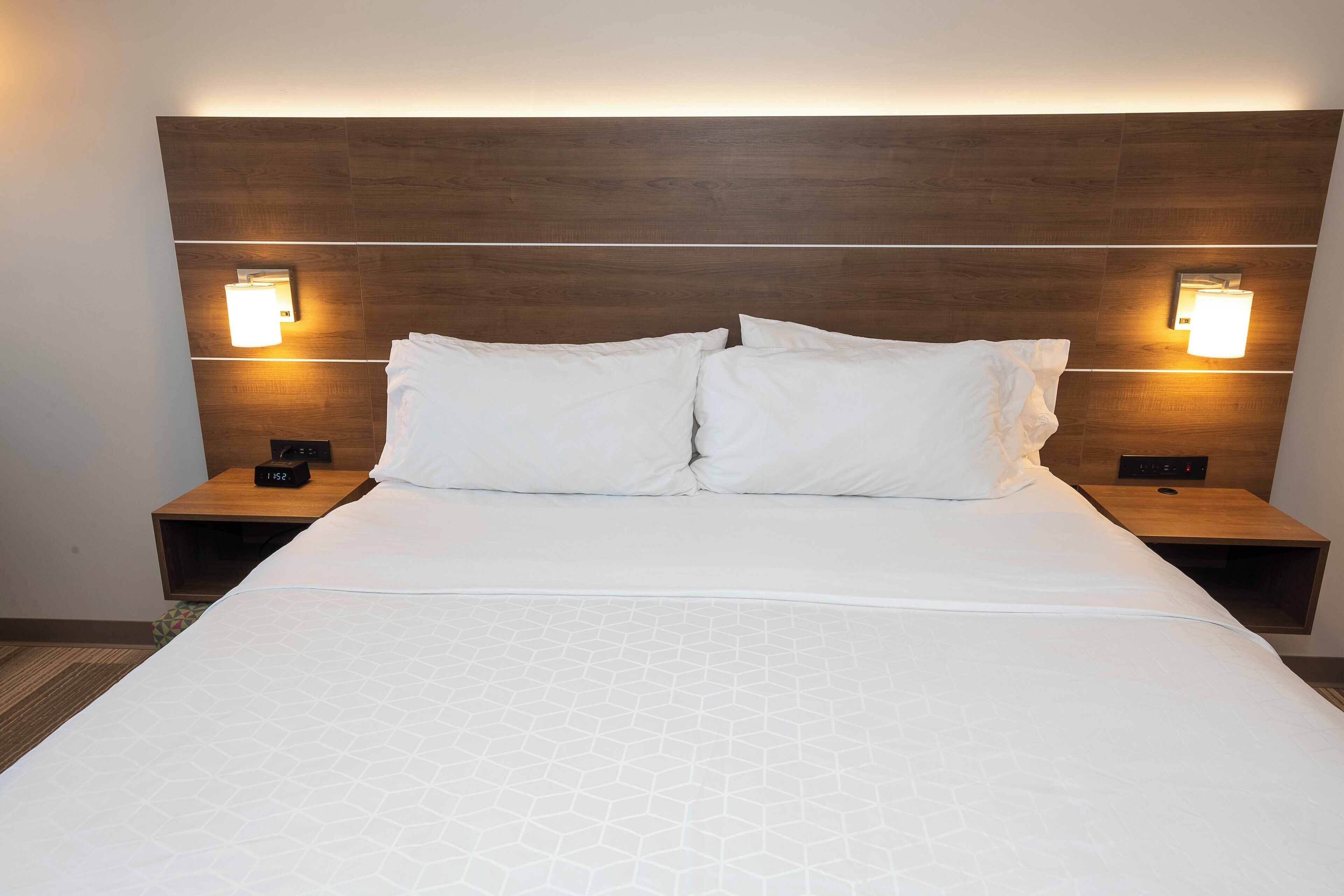 Una habitación de hotel con una cama grande, dos mesitas de noche y lámparas de pared.
