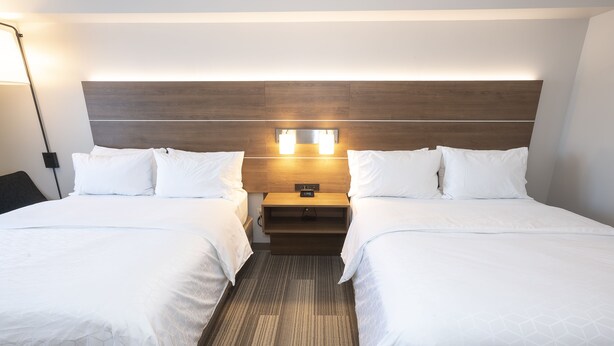 A hotel room with two beds, a wooden headboard, bedside lamps, and a nightstand with a clock. - Holiday Inn Express Hotel & Suites Iron Mountain by IHG (Iron Mountain)