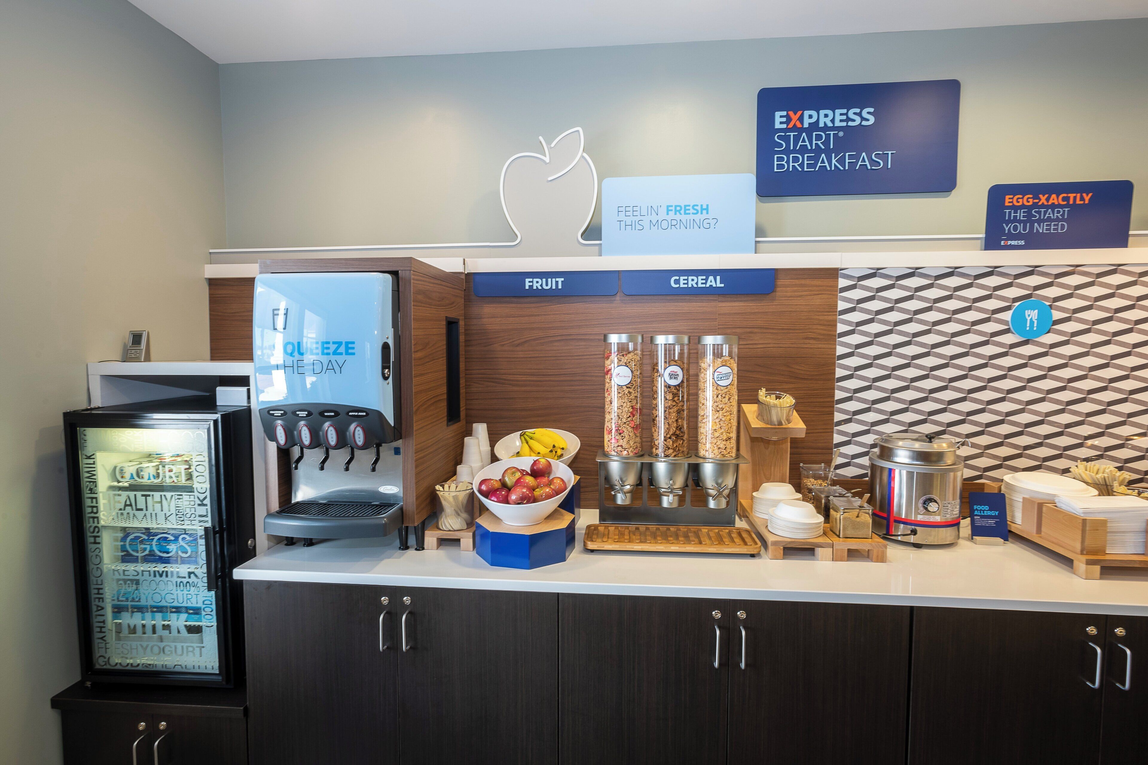 Estación de desayuno con máquina de café, dispensadores de fruta y cereales, y un letrero que indica Desayuno Express.