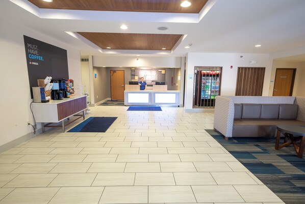 A hotel lobby with a reception desk, a coffee station, a seating area with a sofa, and a vending machine.