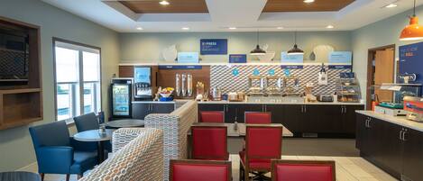 A modern breakfast area with seating, a counter with food options, and a view of the outside.