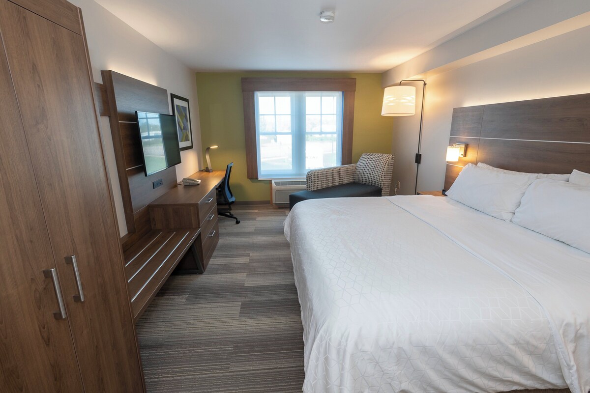 A hotel room with a bed, a desk, a chair, a television, and a window.