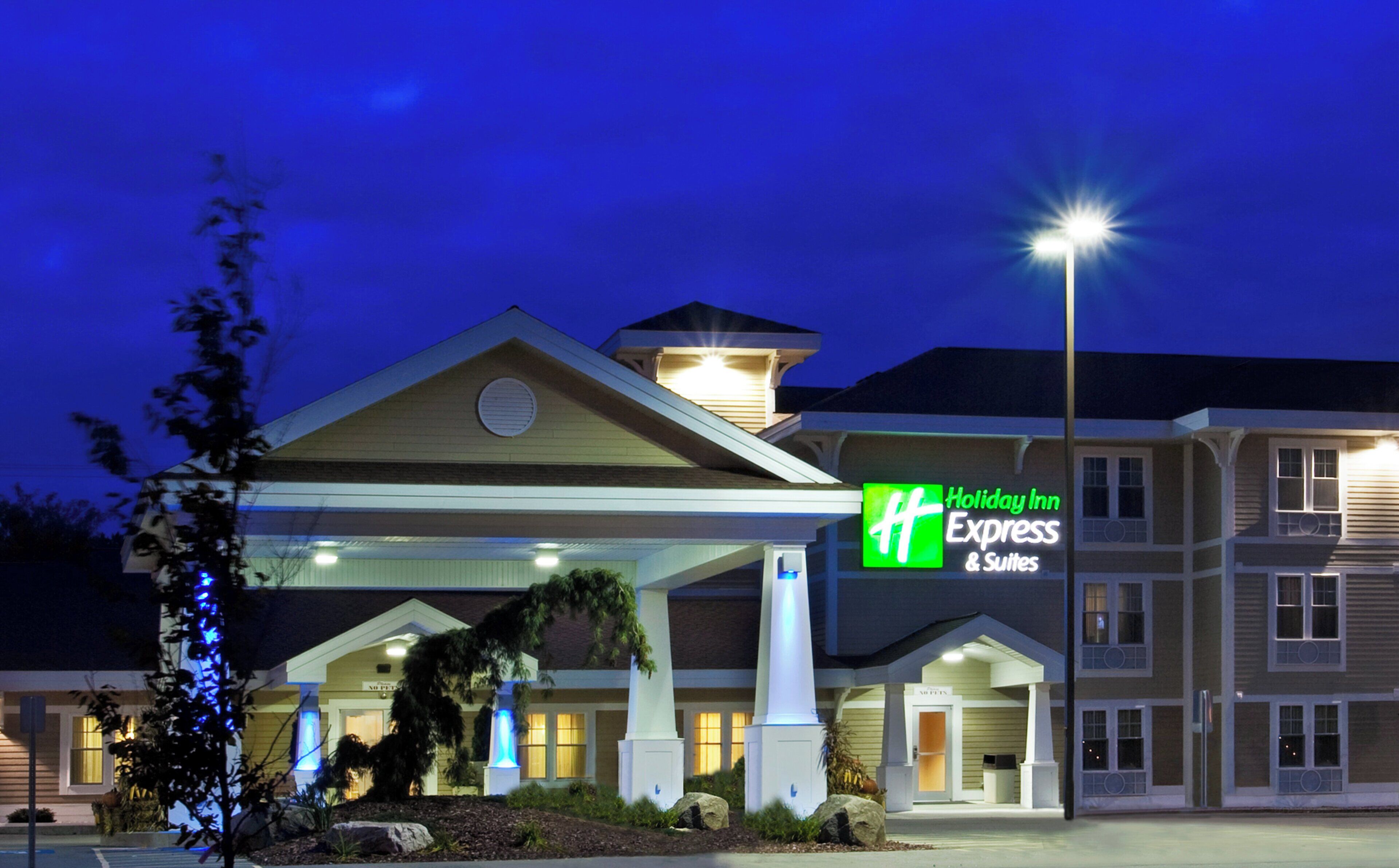 Ein Holiday Inn Express & Suites mit überdachtem Eingang, beleuchtetem Schild und gut ausgeleuchteter Fassade.