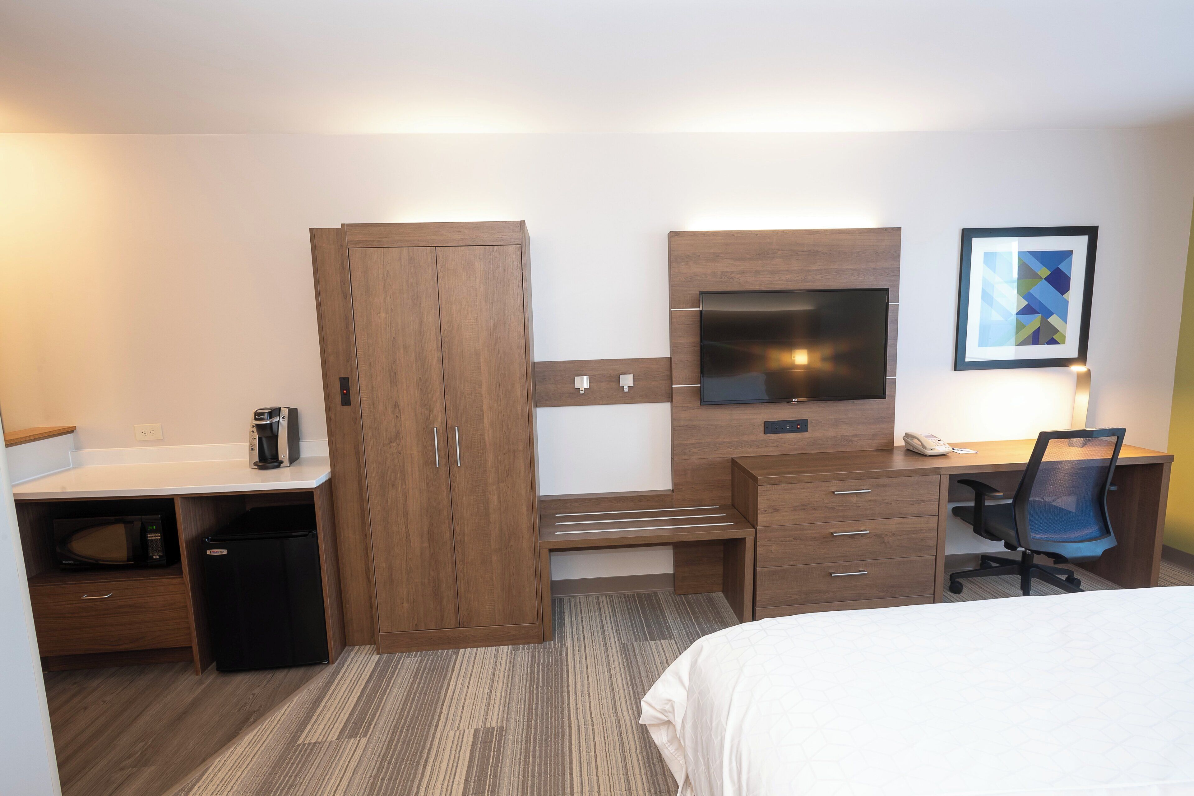 A hotel room with a bed, a desk with a computer, a television, a wardrobe, and a coffee machine.