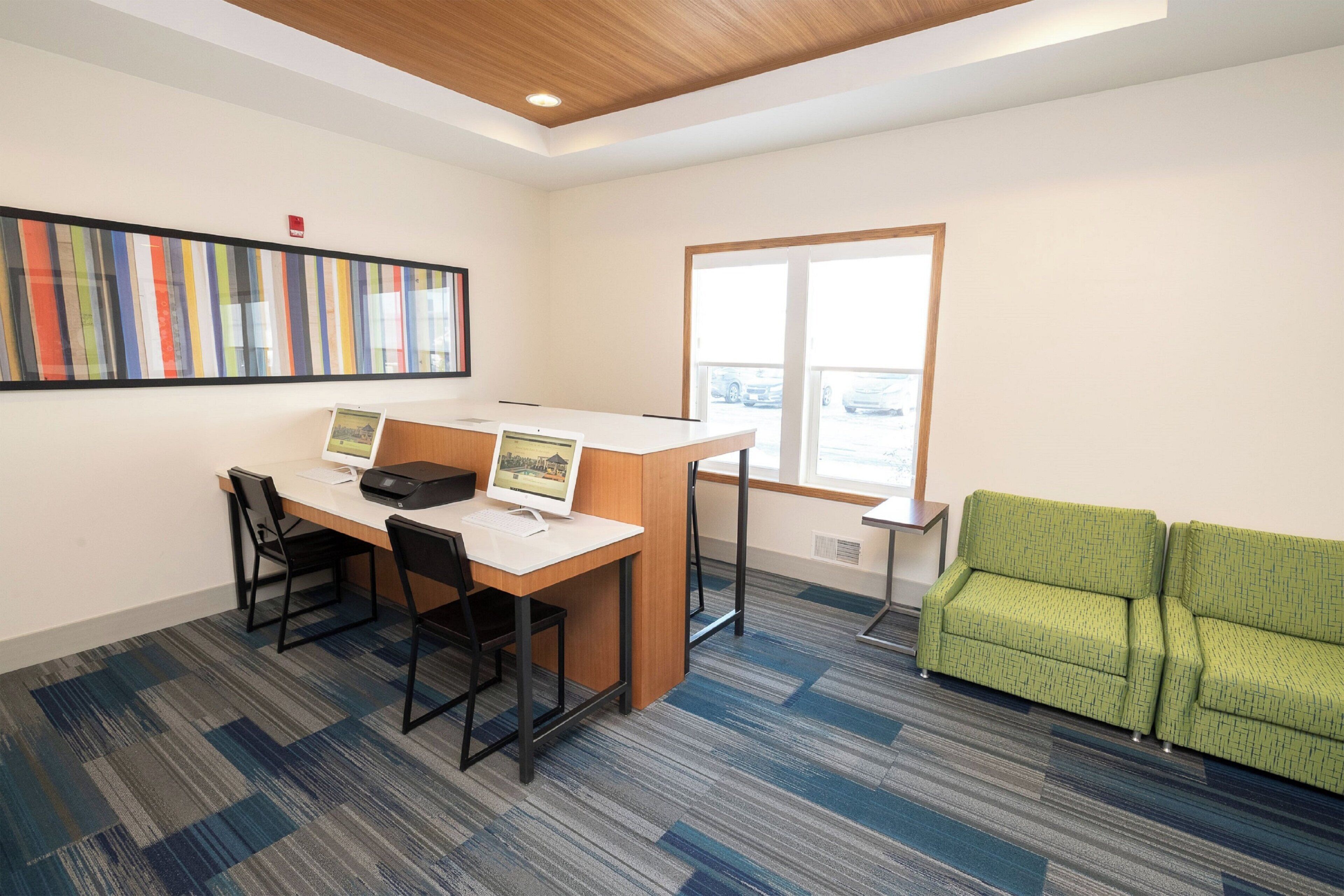 Un espace de bureau moderne comprenant un bureau, deux chaises, un canapé vert et une grande fenêtre.