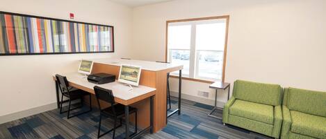 Un espace de bureau moderne comprenant un bureau, deux chaises, un canapé vert et une grande fenêtre.