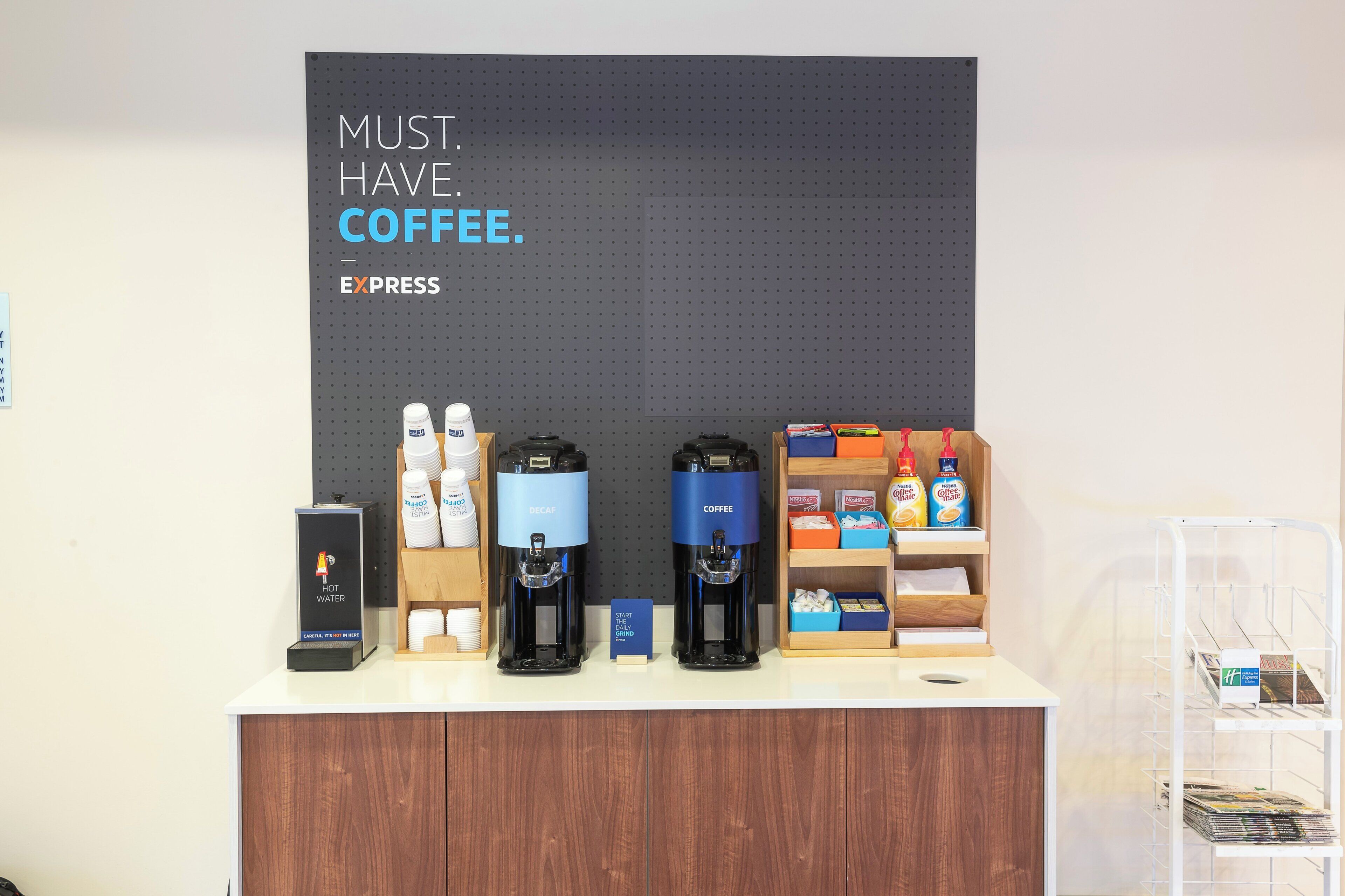 A coffee station with a sign that reads 'MUST HAVE COFFEE.' It includes a coffee machine, a water dispenser, and a display of coffee pods.