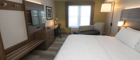 A hotel room with a large bed, a desk, a chair, a flat-screen TV, and a window with blinds.