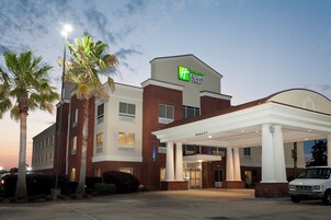 Um hotel Holiday Inn Express & Suites com fachada de tijolos, entrada coberta e palmeiras.
