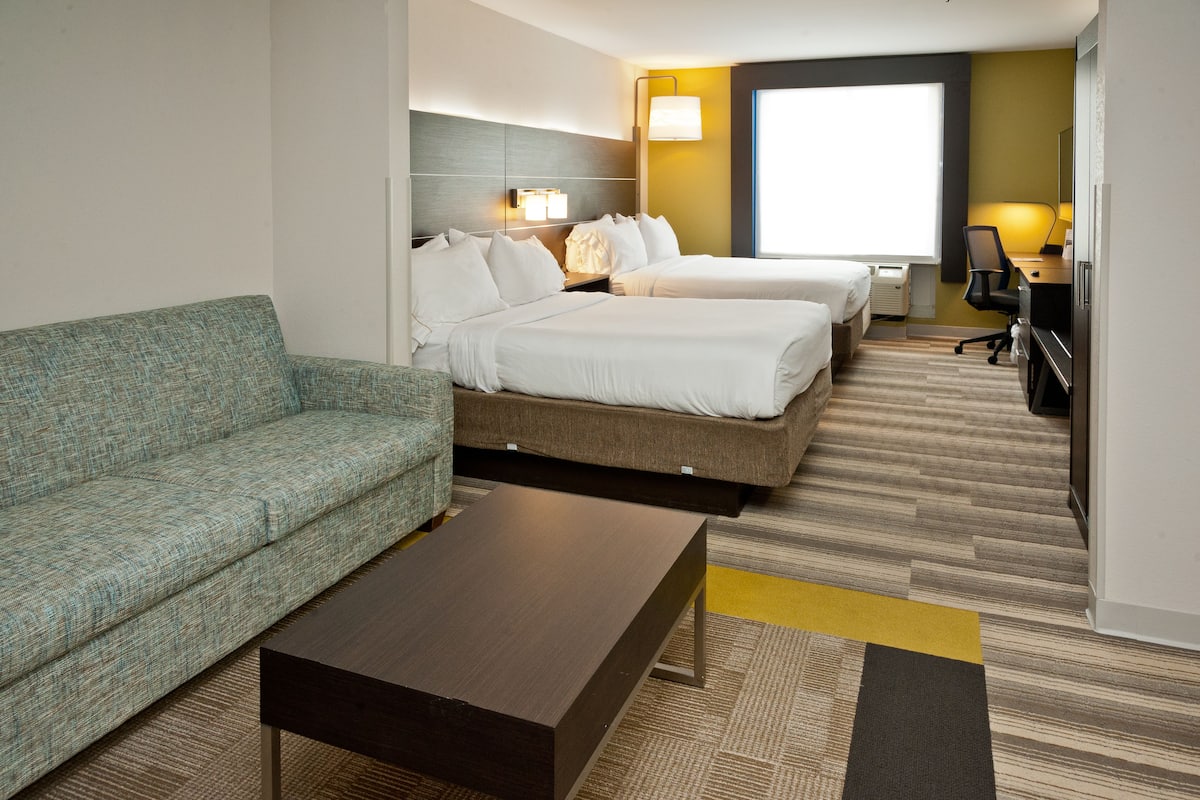 A hotel room with a sofa, two beds, a desk, and a TV.