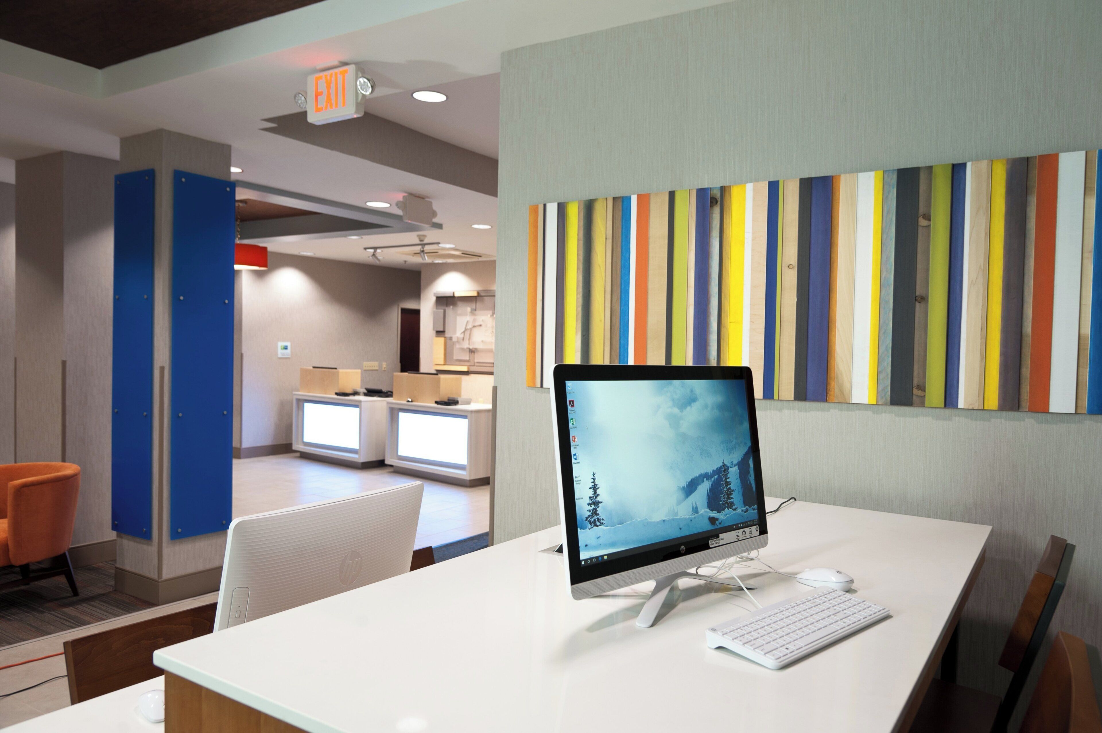 A hotel room with a desk, a computer, and a view of the lobby.