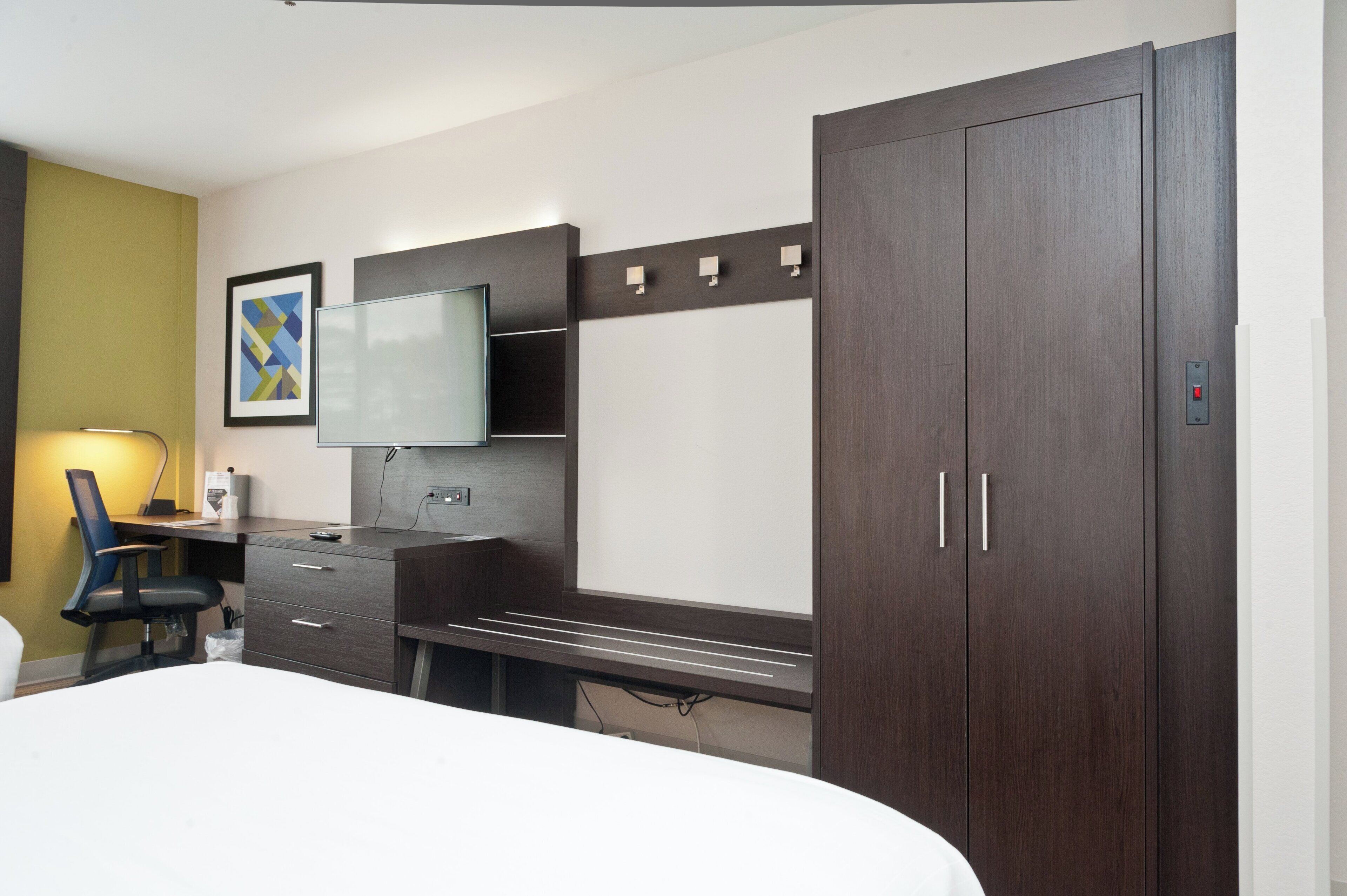 A hotel room with a bed, a desk with a chair, a television, and a wardrobe.
