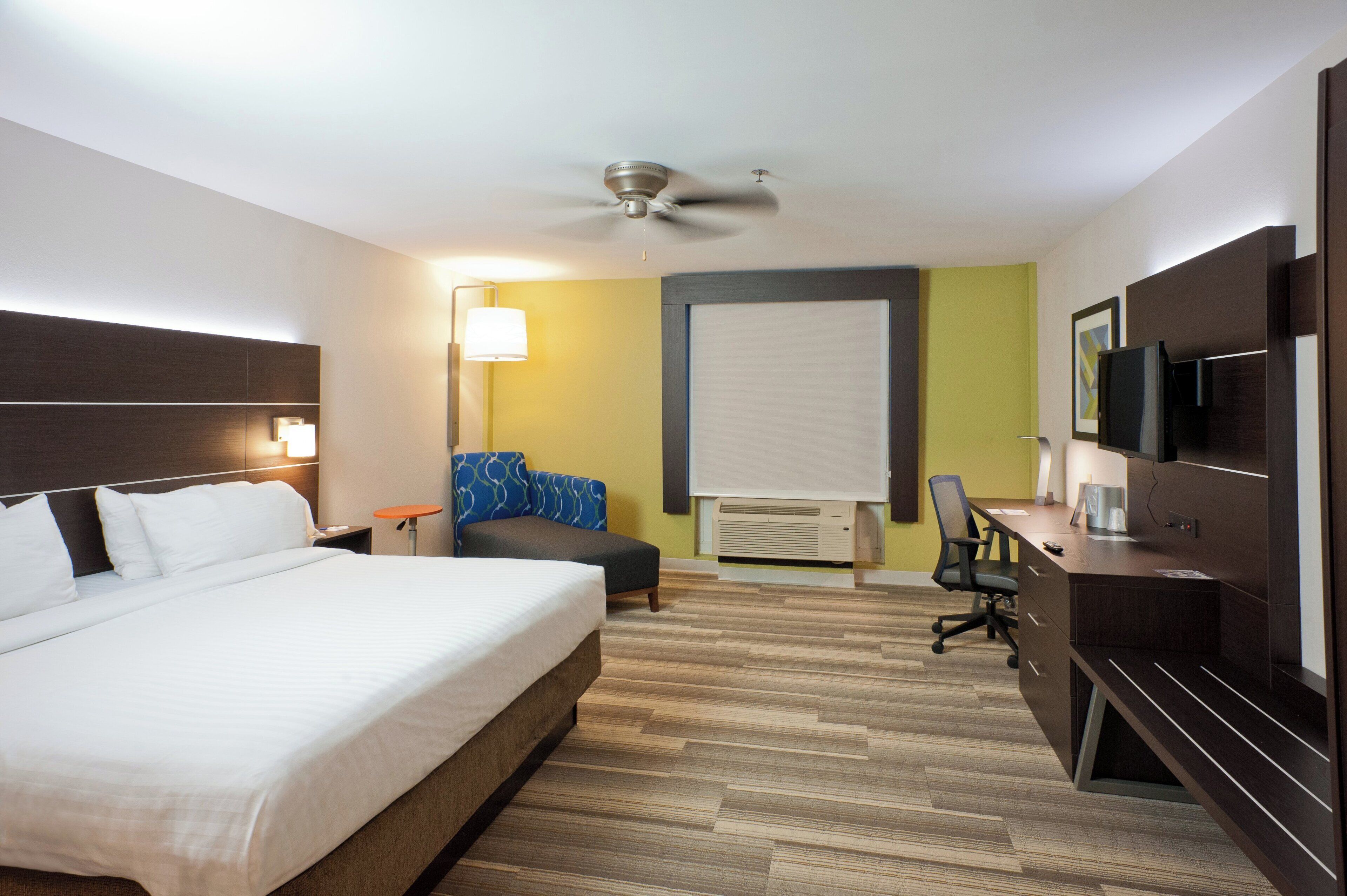 A hotel room with a bed, a desk, a chair, a television, and a ceiling fan.