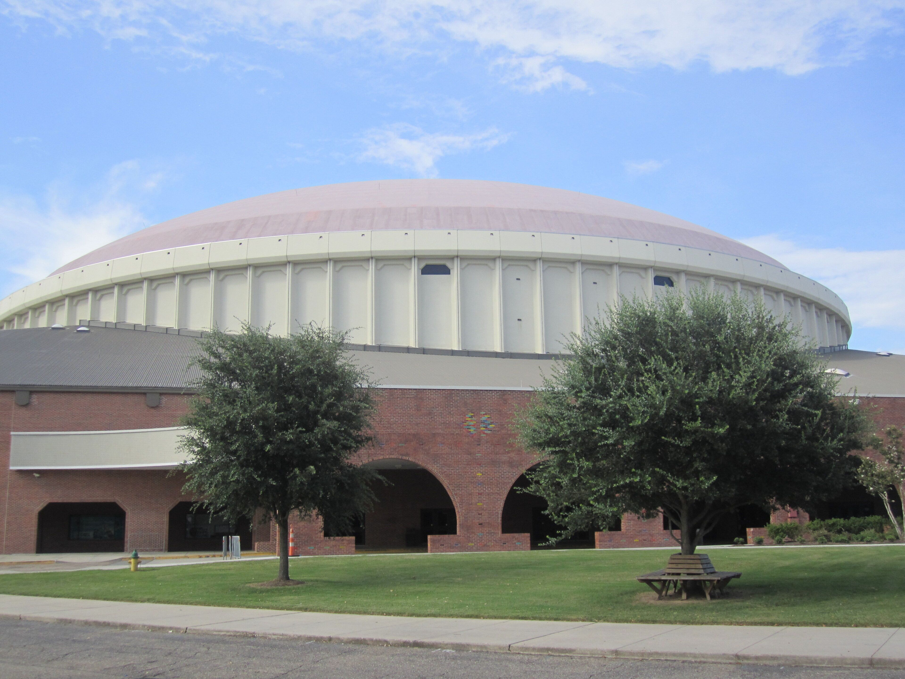 A large, circular building with a dome roof, surrounded by a grassy area and a few trees.