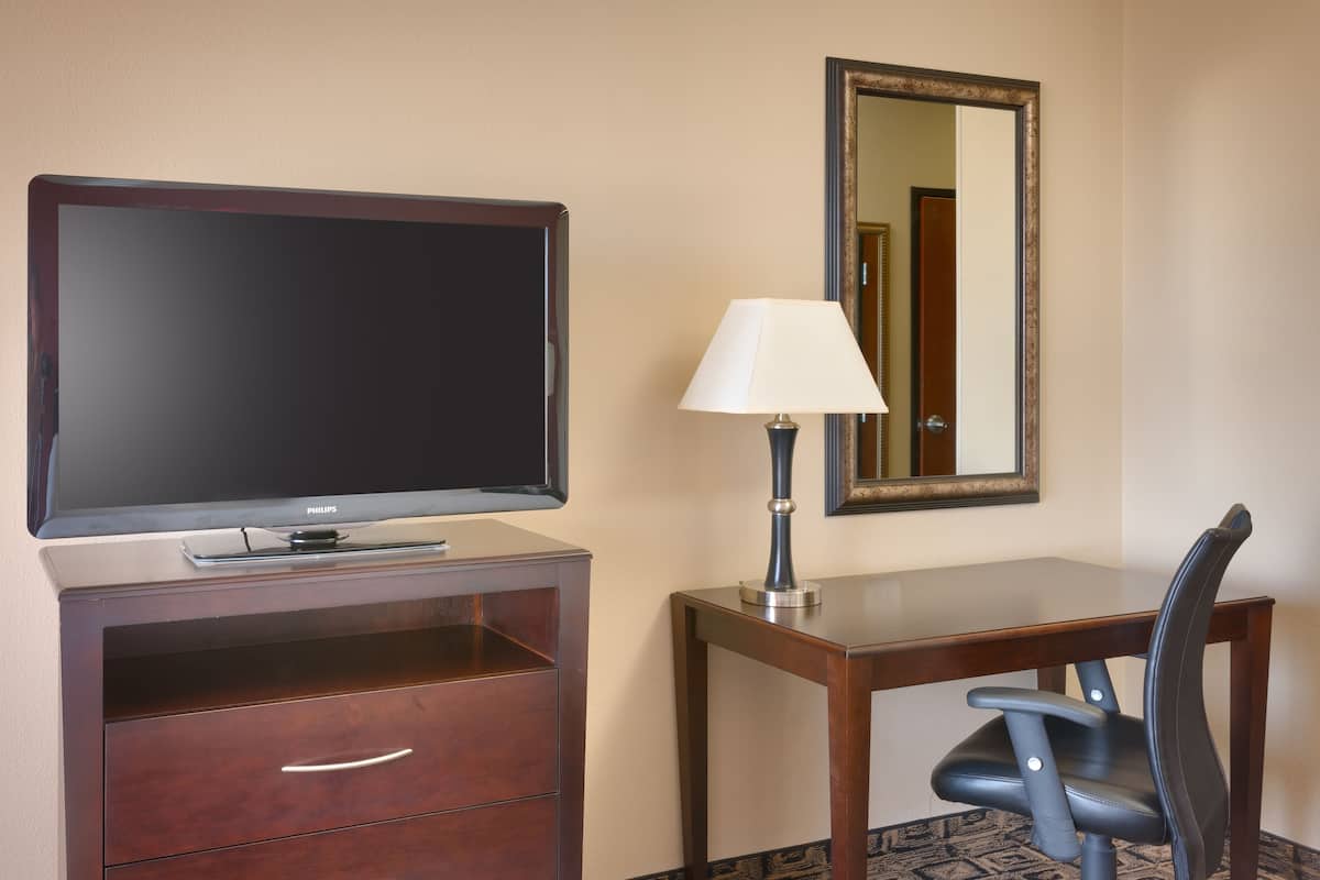 Une chambre d’hôtel équipée d’une télévision à écran plat, d’un bureau avec une lampe, d’une chaise et d’un miroir mural.