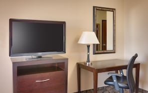 Ein Hotelzimmer mit Fernseher, Schreibtisch mit Lampe, Stuhl und Spiegel an der Wand.