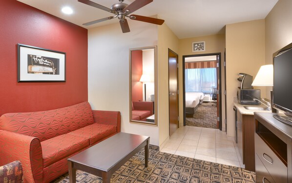 Habitación de hotel con sofá rojo, una mesita, ventilador de techo, televisión y un espejo que refleja la habitación.