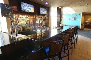A bar area with a long counter, multiple TVs, and a variety of bottles.