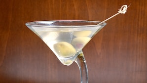 Um copo de martini com uma fatia de limão sobre uma superfície branca, com um fundo de madeira.
