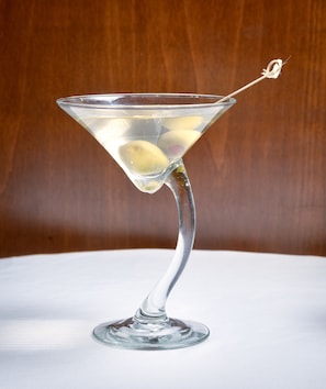 Ein Martini-Glas mit Zitronenscheibe auf weißer Oberfläche vor Holz im Hintergrund.