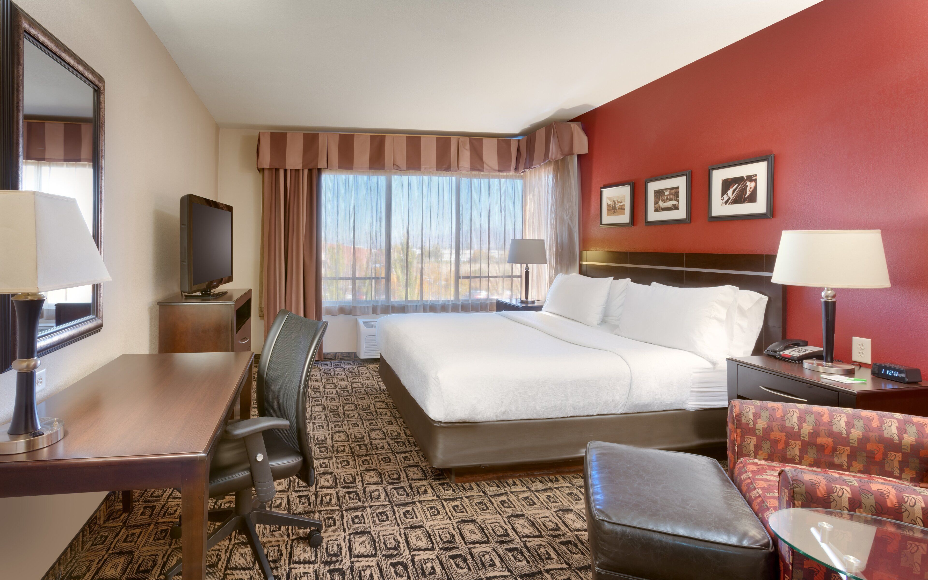 A hotel room with a bed, desk, chair, television, and a view of the outdoors.