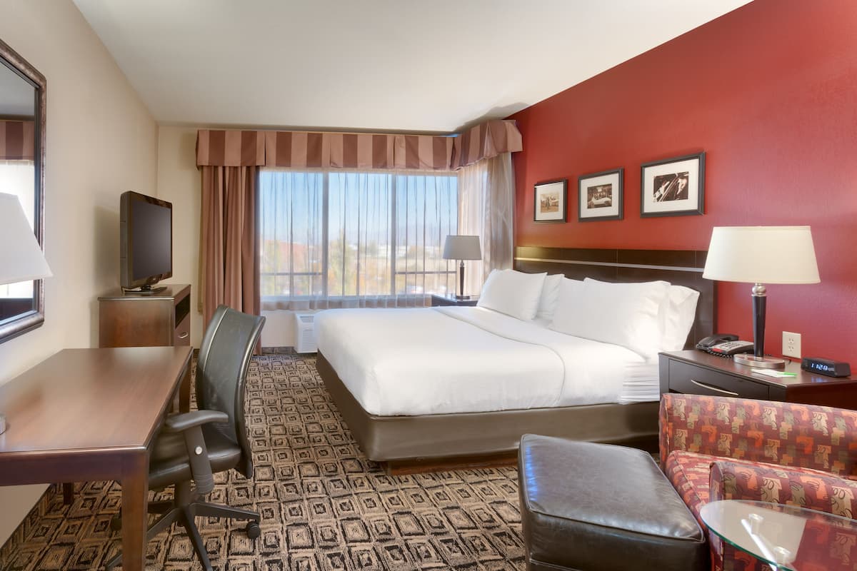 Une chambre d’hôtel avec un grand lit, un bureau avec une chaise, une télévision, une lampe de bureau, une horloge et une moquette à motifs.