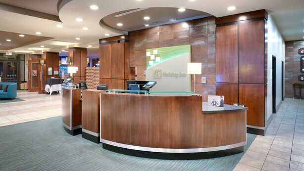 Uma área de recepção de hotel com um balcão de madeira, uma divisória de vidro e a placa "Holiday Inn".