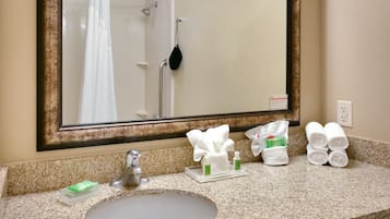 Un baño con lavamanos, espejo, ducha y toallero.
