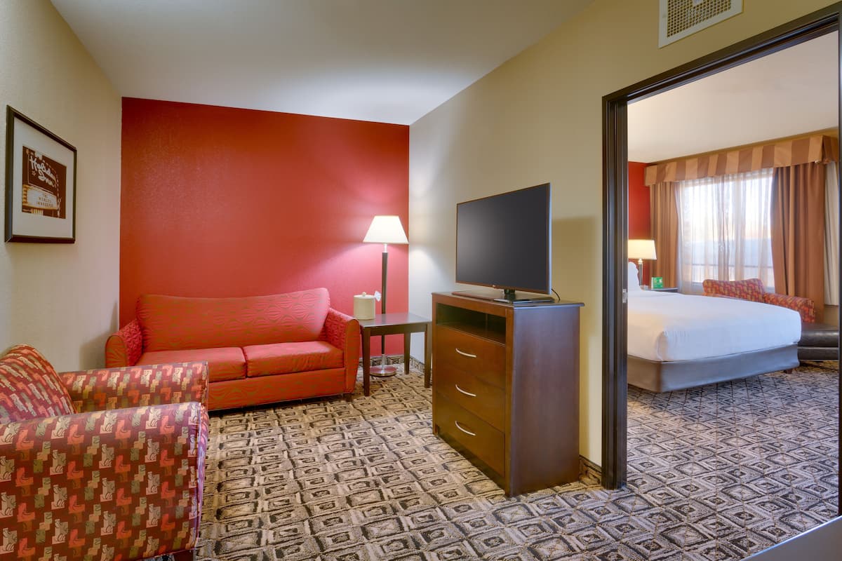 Une chambre d’hôtel avec un mur rouge, un canapé, une télévision, une commode et un lit.