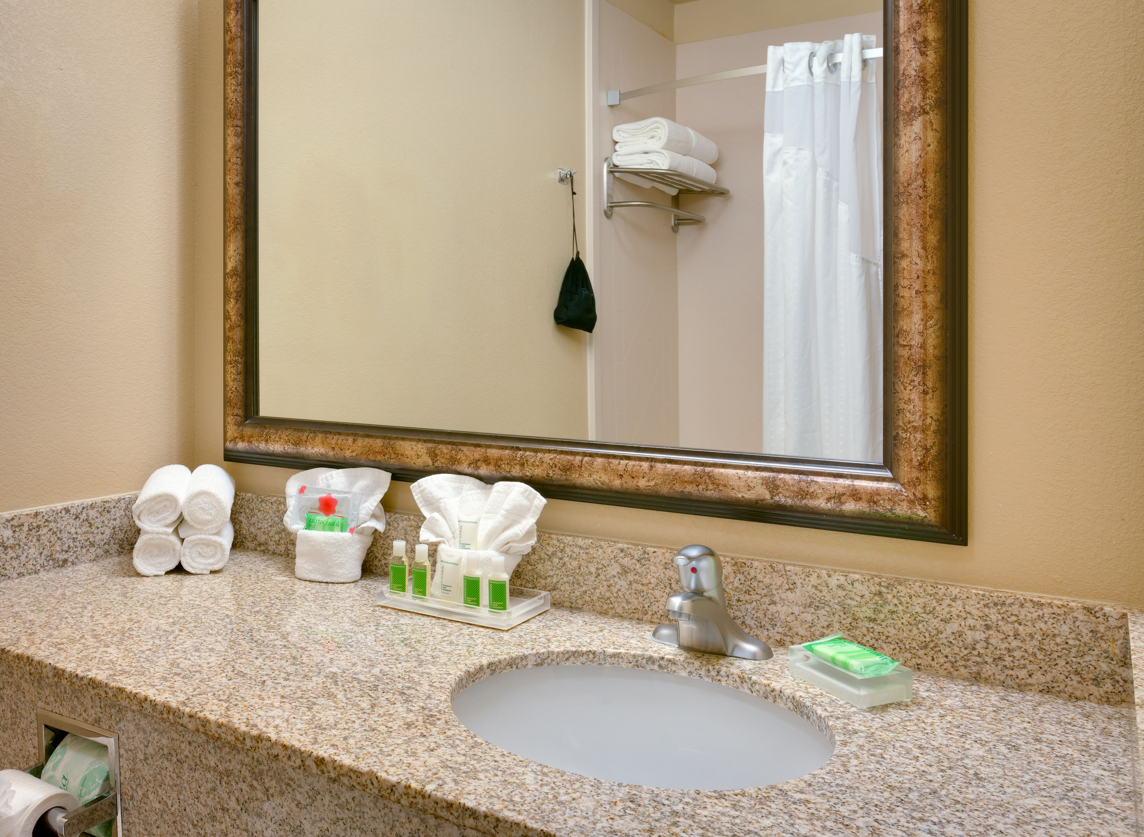 Une salle de bain avec un comptoir en granit, un lavabo, un miroir et des articles de toilette.