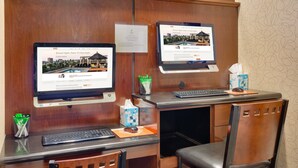 A hotel reception desk with two monitors displaying the hotel's website, a keyboard, a mouse, a tissue box, and a pen holder.