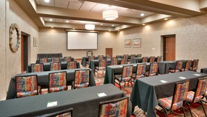 A conference room with rows of tables and chairs, a projector screen, and a large window with a view.