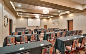 A conference room with rows of tables and chairs, a projector screen, and a large window with a view.