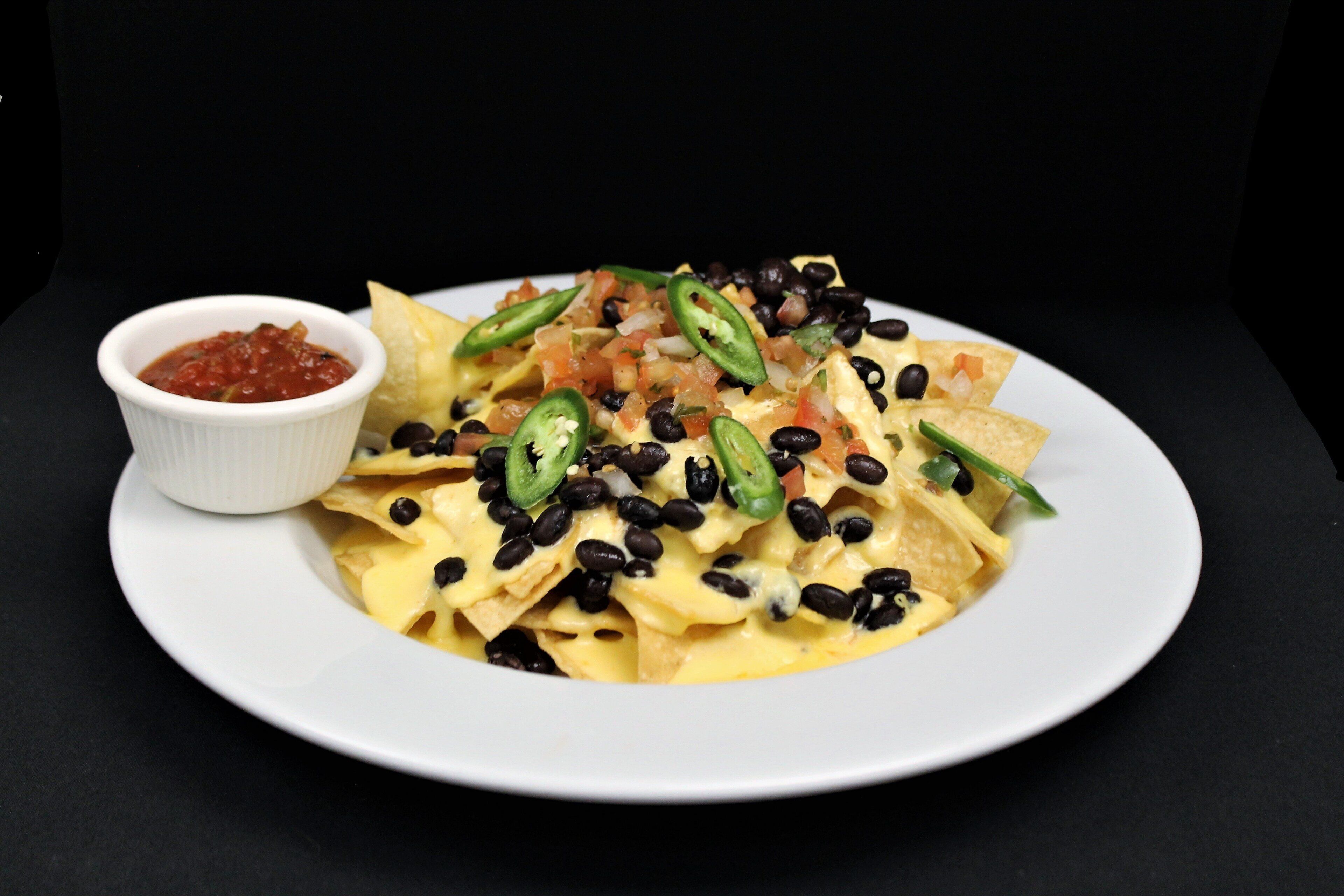 A plate of nachos topped with cheese, black beans, jalapeños, and a side of salsa.