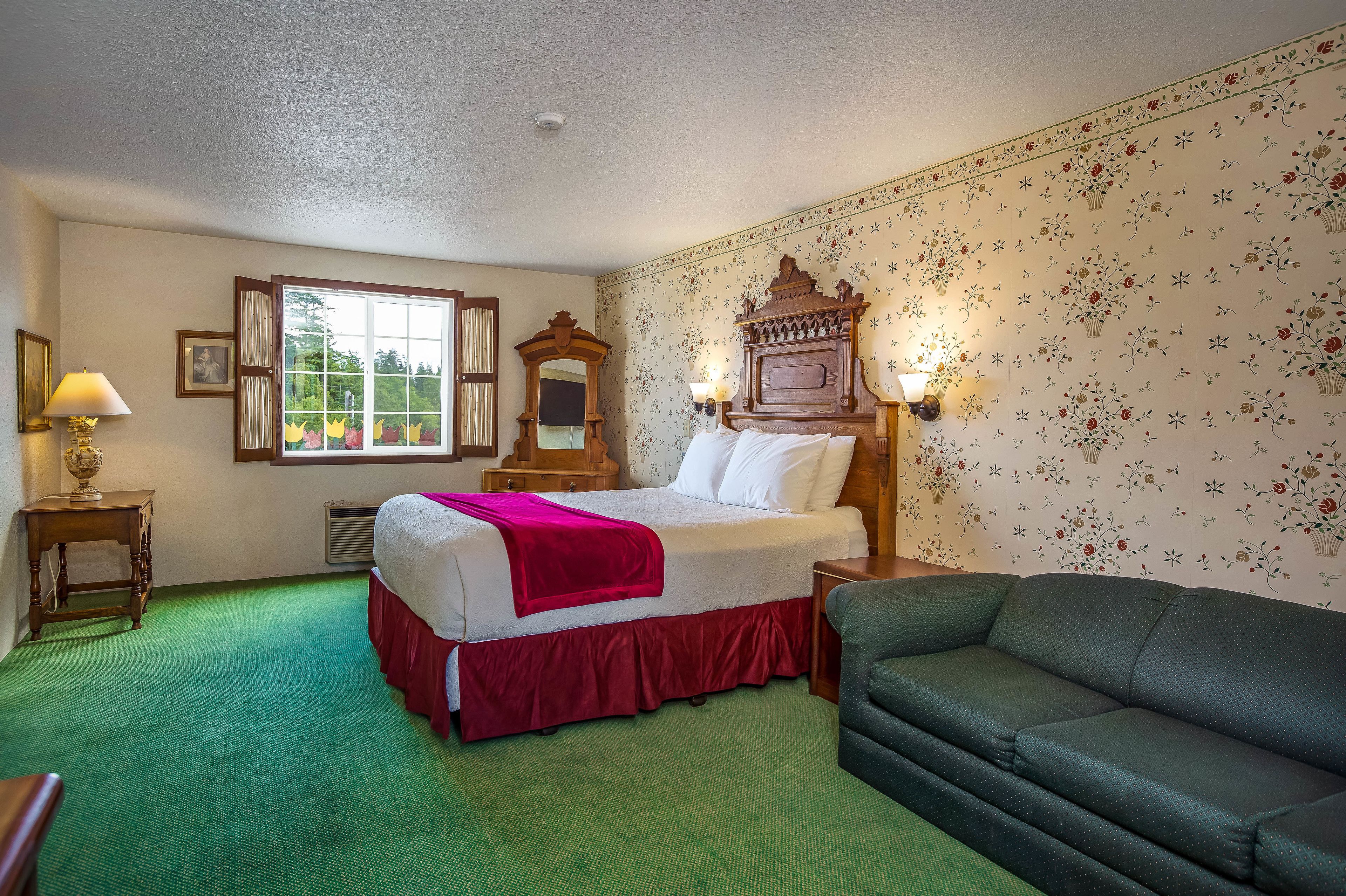 A hotel room with a bed, green carpet, floral wallpaper, and a green sofa.