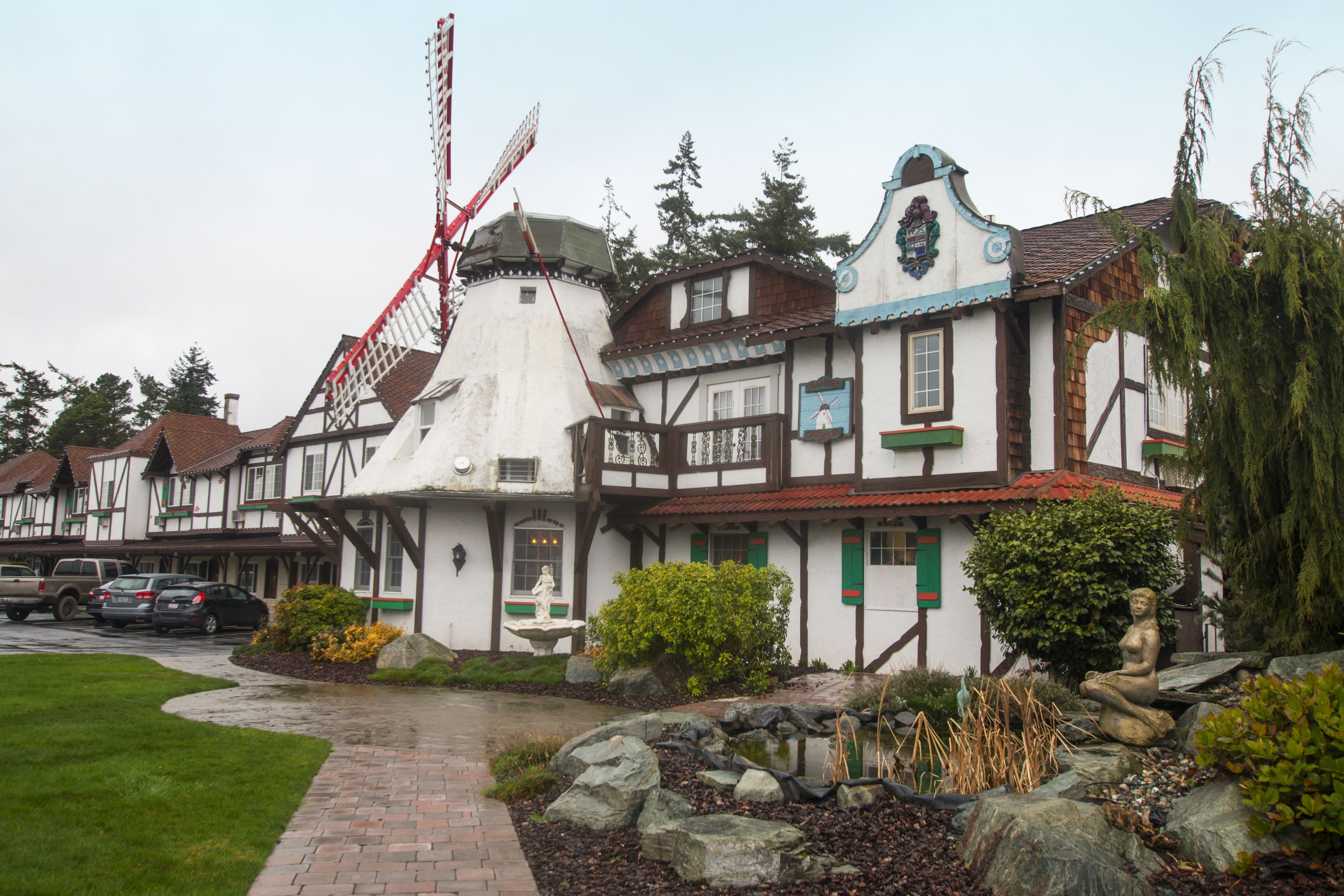 A traditional European-style building with a windmill, stone pathway, and a statue in the garden.