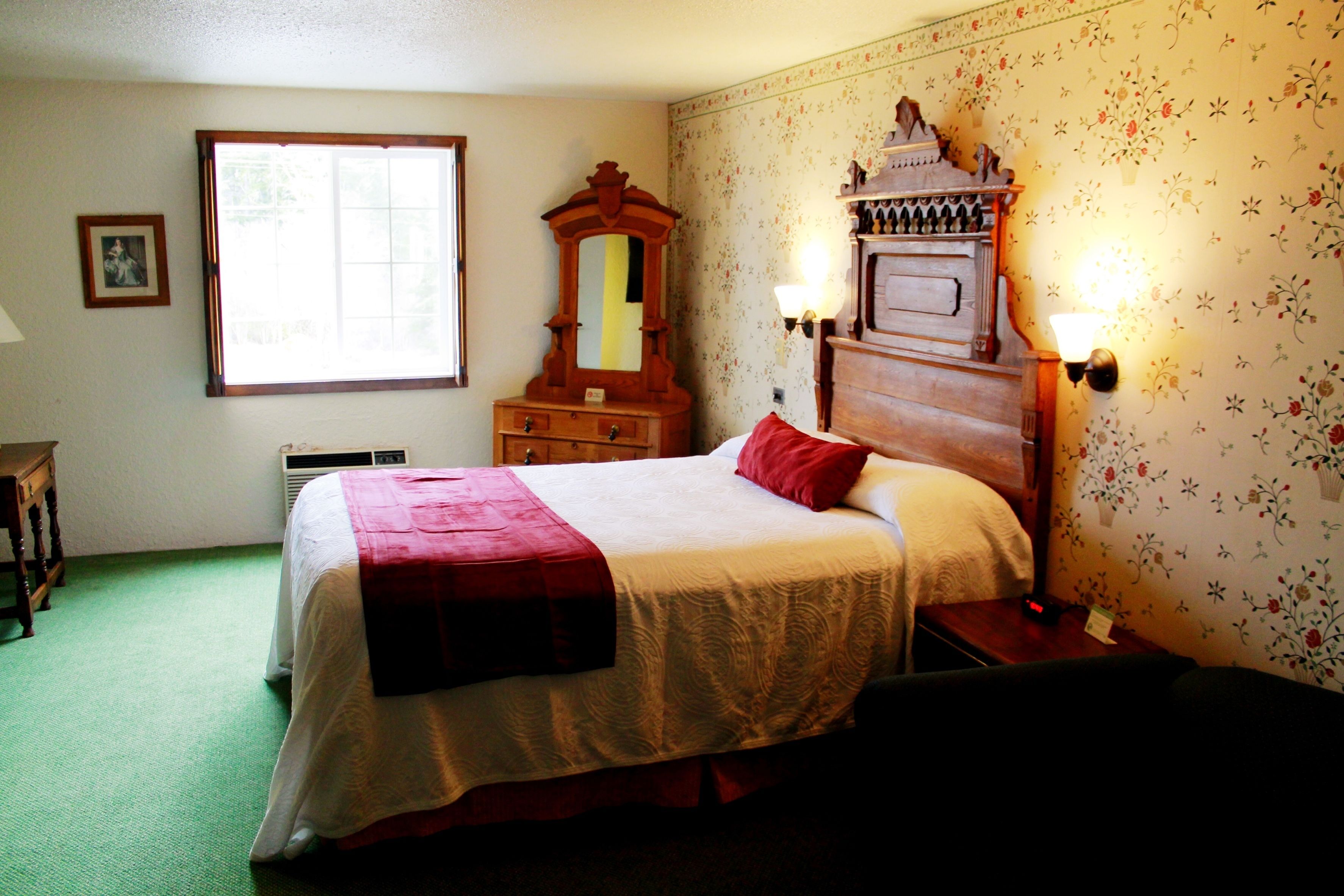 Une chambre à coucher comprenant un lit, une commode, un miroir et deux appliques murales.