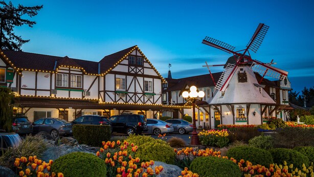 A traditional half-timbered building with a windmill, surrounded by a well-maintained garden with tulips. - Auld Holland Inn (Oak Harbor)