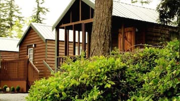 A rustic wooden cabin with a porch and a large tree in front.