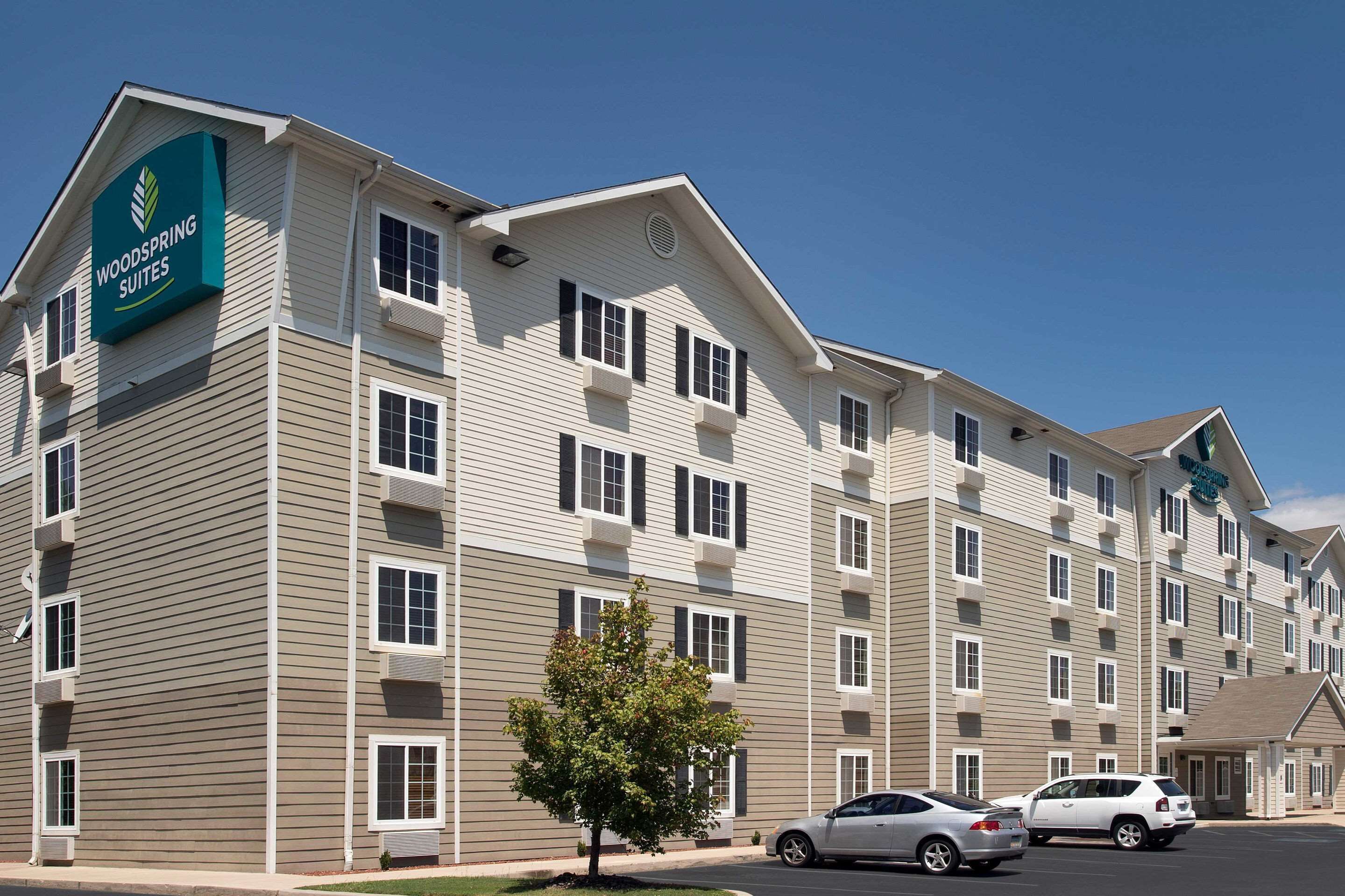 A multi-story hotel with a sign reading "Woodspring Suites." It features a symmetrical facade with evenly spaced windows and balconies.