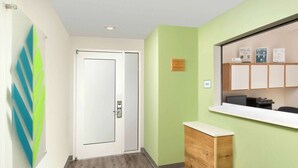 A reception area with a wooden counter, a glass door, and a wall-mounted information board.
