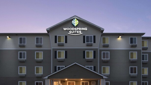 A multi-story hotel with a flat roof, a central entrance, and a sign reading "Woodspring Suites".