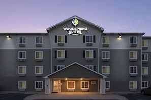 Un hotel de varios pisos con techo plano, entrada central y un letrero que dice "Woodspring Suites".