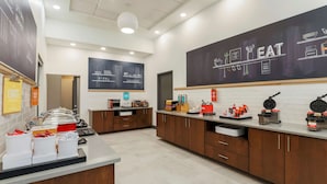 A modern kitchen area with a buffet setup, including a counter with food containers and a chalkboard menu. - Hampton Inn & Suites Pittsburgh-Downtown (Pittsburgh)