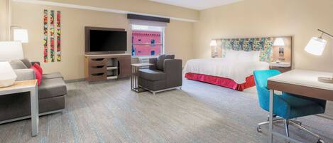 A hotel room with a bed, a desk, a chair, a TV, and a sofa.