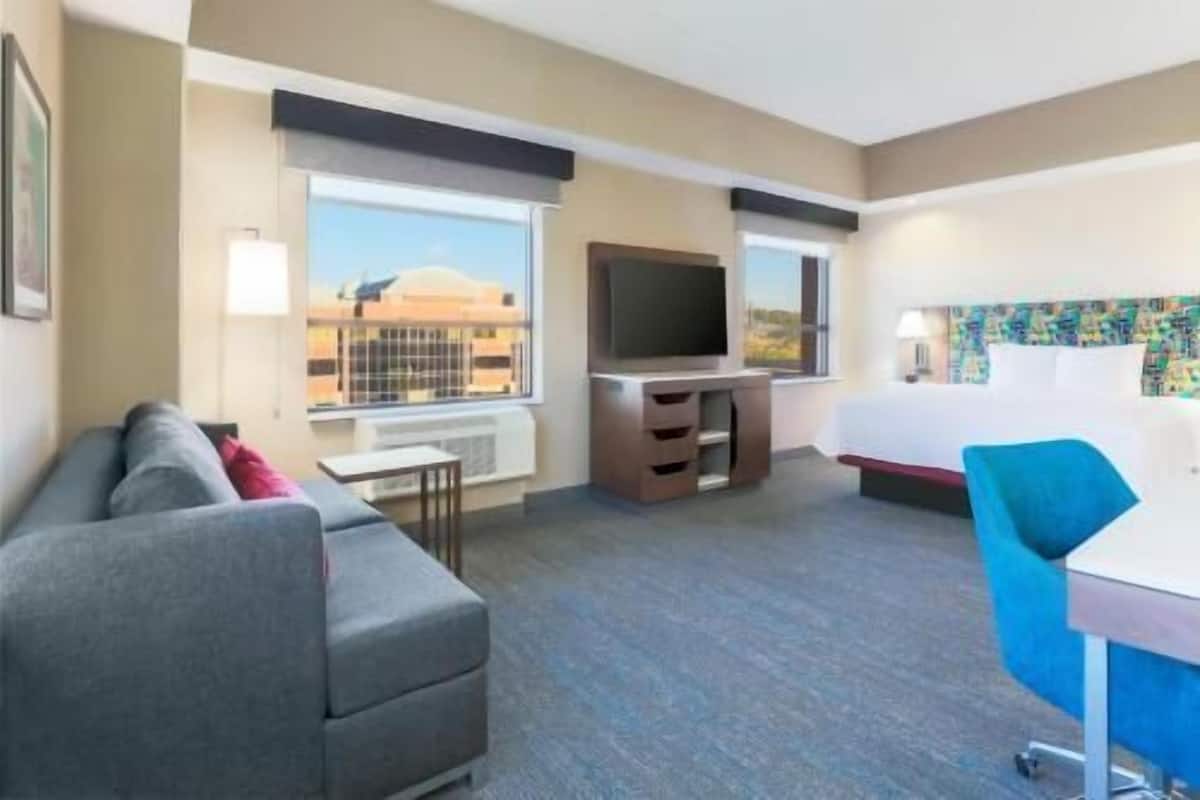 Quarto de hotel com sofá, televisão, cama e escrivaninha.