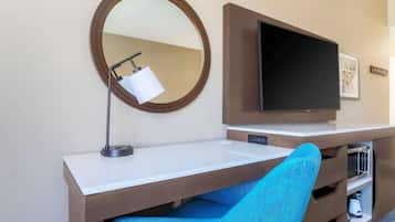 Een hotelkamer met een bureau, een televisie, een spiegel en een blauwe stoel.