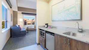 A compact kitchen with a built-in microwave, dishwasher, and a sink. There's a gray sofa in the adjacent living area, and a large framed artwork on the wall. - Hampton Inn & Suites Pittsburgh-Downtown (Pittsburgh)